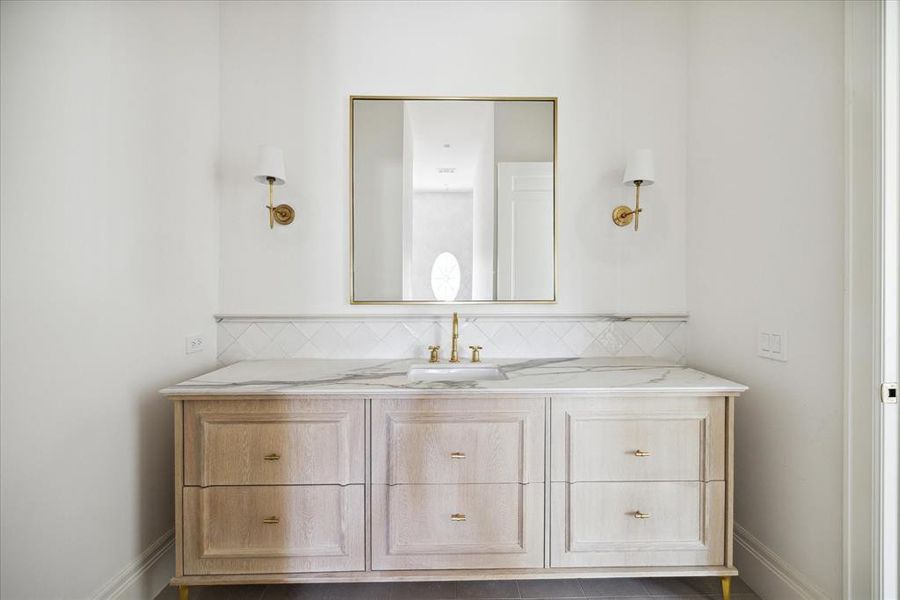 This secondary bathroom features wall mounted sconces, a white oak vanity, and porcelain under-mount sink with gold fixtures.