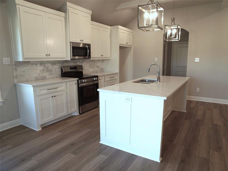 Kitchen featuring decorative light fixtures, a center island with sink, appliances with stainless steel finishes, sink, and white cabinets