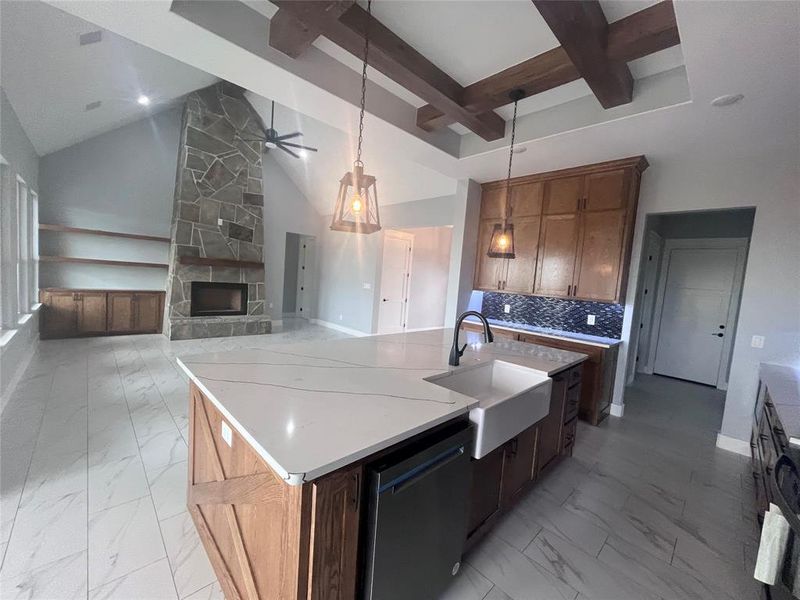 Kitchen featuring a kitchen island with sink, dishwasher, beamed ceiling, a fireplace, and sink