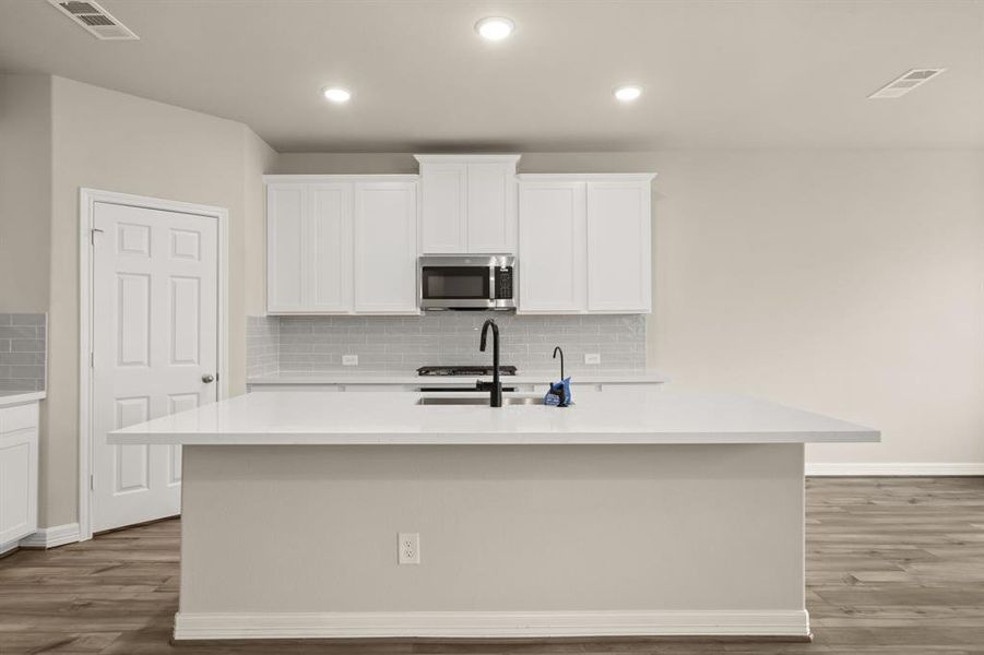 This light and bright kitchen features a large quartz island, white cabinets, a large sink overlooking your family room, recessed lighting, and beautiful backsplash.