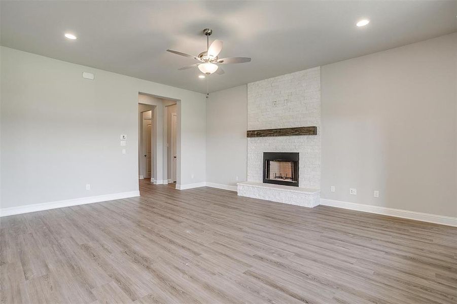 Unfurnished living room with brick wall, a fireplace, light wood-type flooring, and ceiling fan