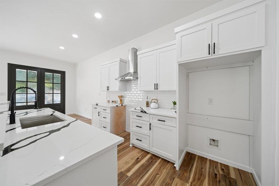 Kitchen featuring backsplash, white cabinetry, wood-type flooring, and wall chimney range hood