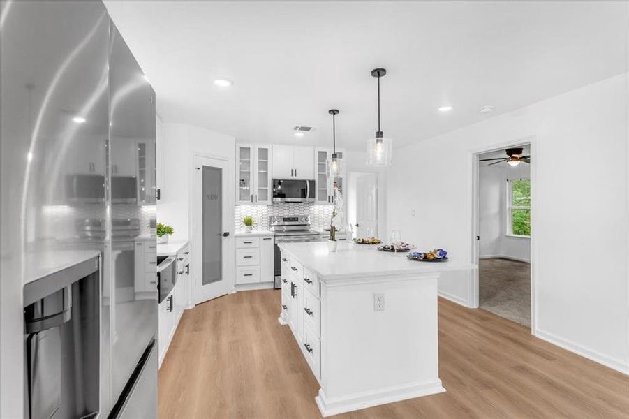 Kitchen featuring ceiling fan, light hardwood / wood-style floors, an island with sink, white cabinetry, and appliances with stainless steel finishes