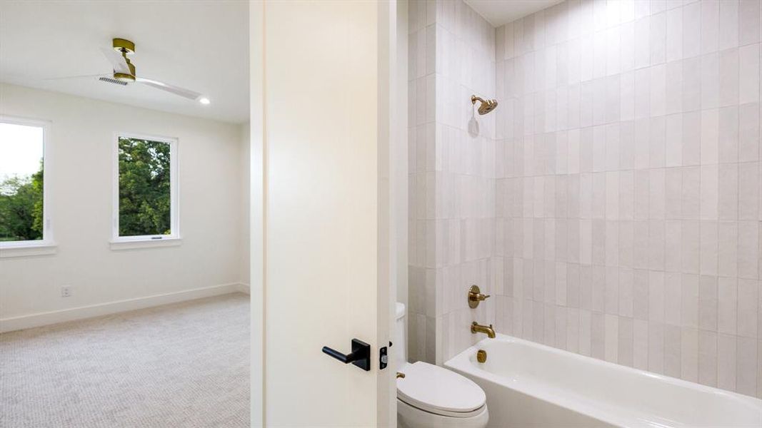 Bathroom featuring toilet, tiled shower / bath, and ceiling fan