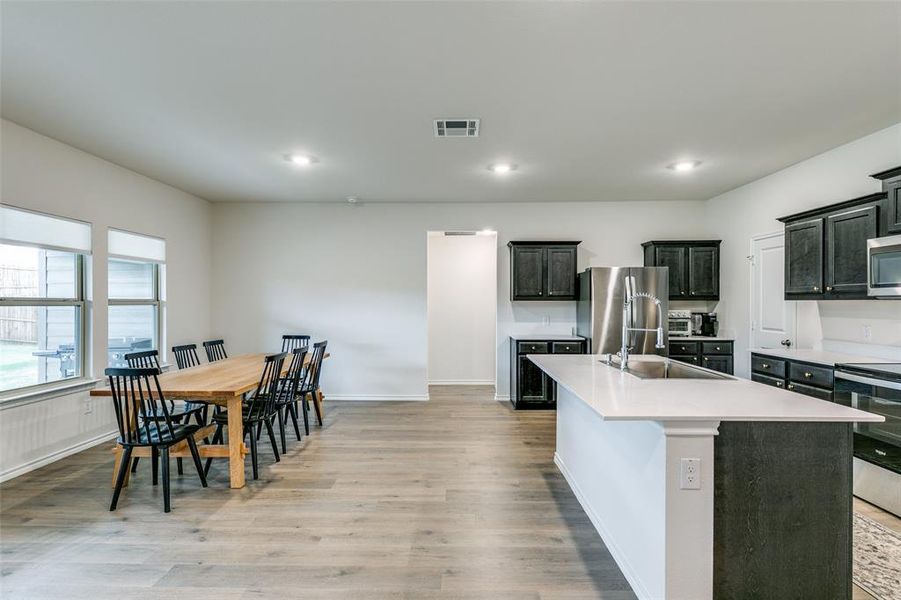 Kitchen with light hardwood / wood-style floors, stainless steel appliances, sink, and a kitchen island with sink