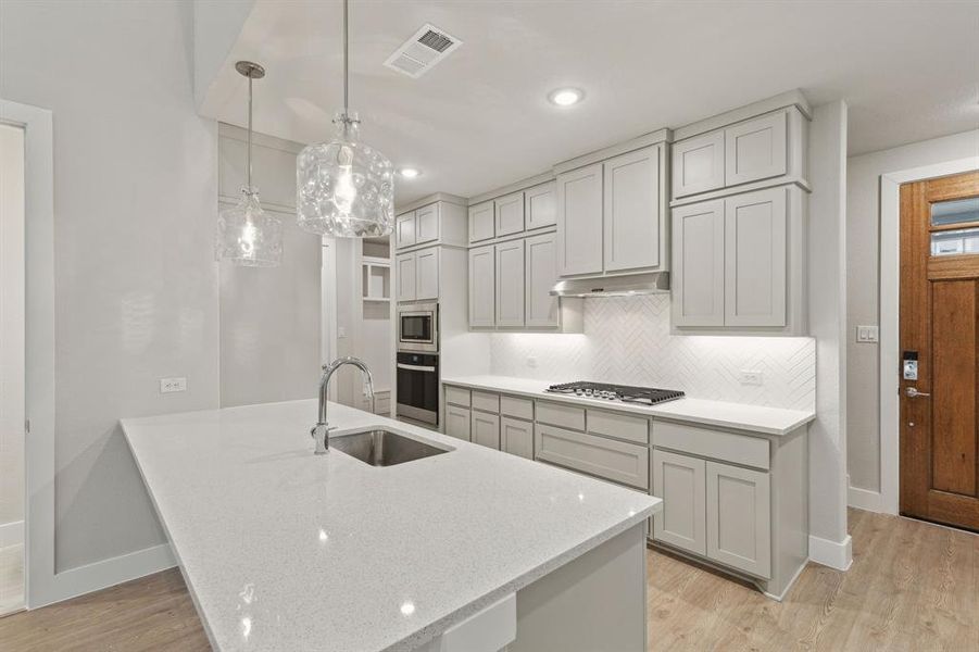 Kitchen featuring decorative light fixtures, stainless steel appliances, light hardwood / wood-style floors, and sink