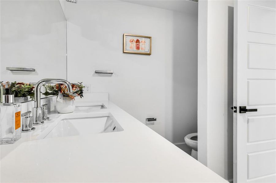 Bathroom with dual sinks, toilet, and vanity with extensive cabinet space