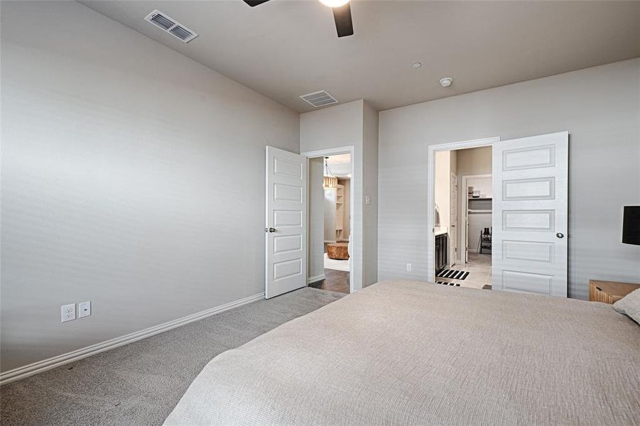 Spacious, carpeted primary bedroom with ceiling fan and bay window