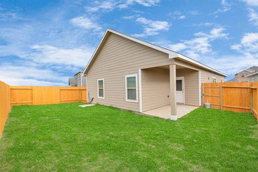 A spacious backyard featuring a beautifully maintained lawn and privacy fence, perfect for outdoor gatherings, relaxation, or gardening. The side view of the house showcases a modern, clean design with beige siding and white trim. This cozy setup provides ample space for family activities or pets to roam freely. **This image is from another Saratoga Home - Wren floor.