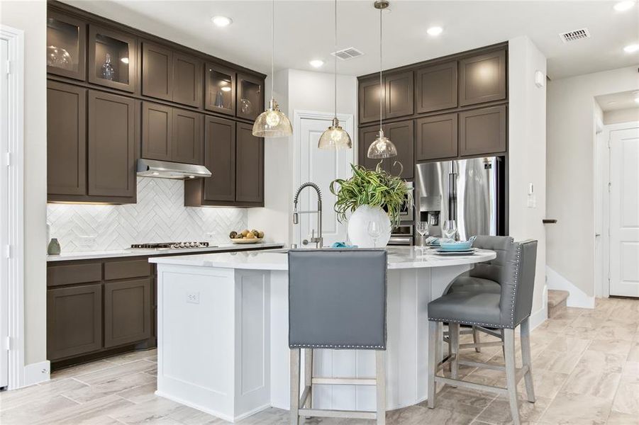 Kitchen featuring decorative light fixtures, dark brown cabinetry, backsplash, a kitchen island with sink, and appliances with stainless steel finishes