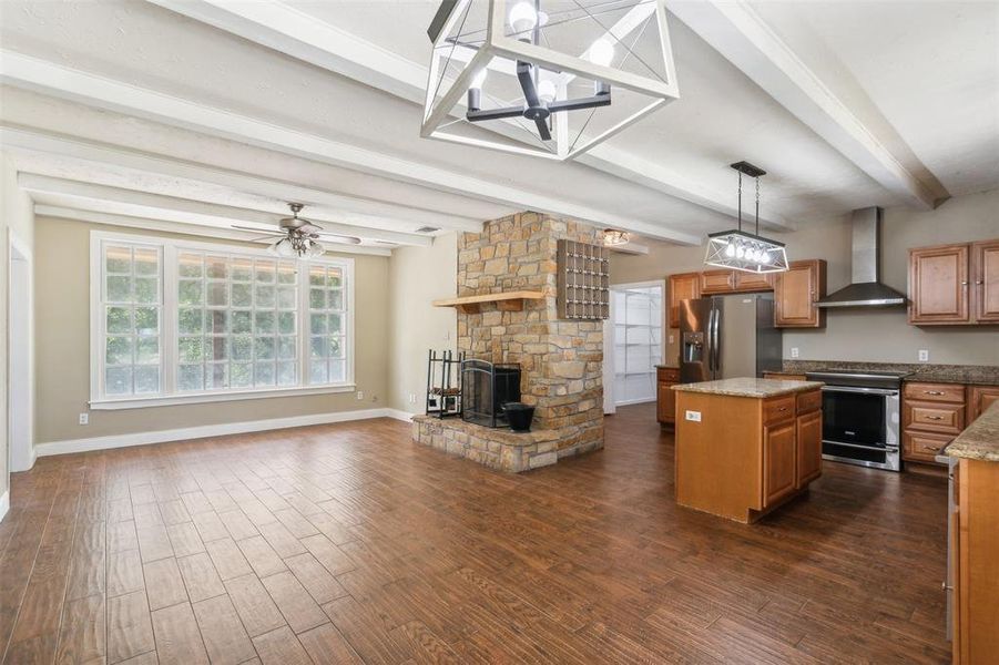 Kitchen featuring stainless steel appliances, dark hardwood / wood-style flooring, wall chimney exhaust hood, a center island, new light fixtures and beam ceiling