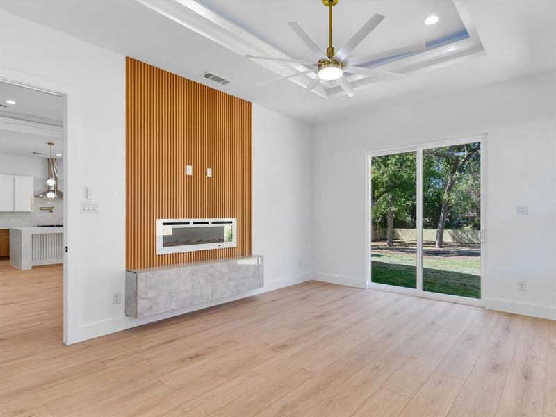 Unfurnished living room featuring light hardwood / wood-style flooring, ceiling fan, a raised ceiling, and a fireplace