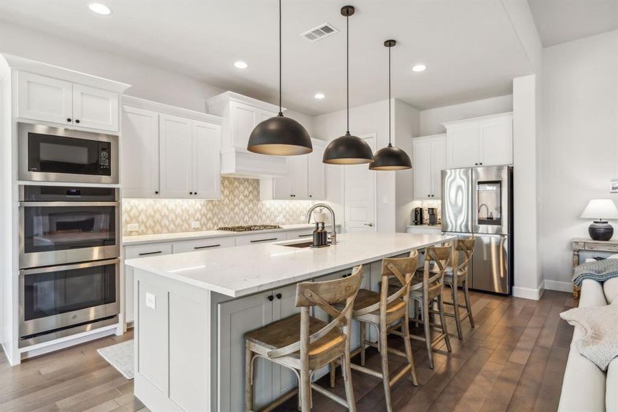 Kitchen with stainless steel appliances, white cabinetry, hanging light fixtures, and sink