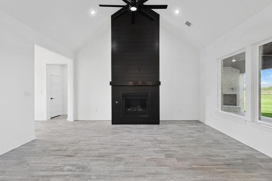 Unfurnished living room with high vaulted ceiling, ceiling fan, a large fireplace, and light hardwood / wood-style floors