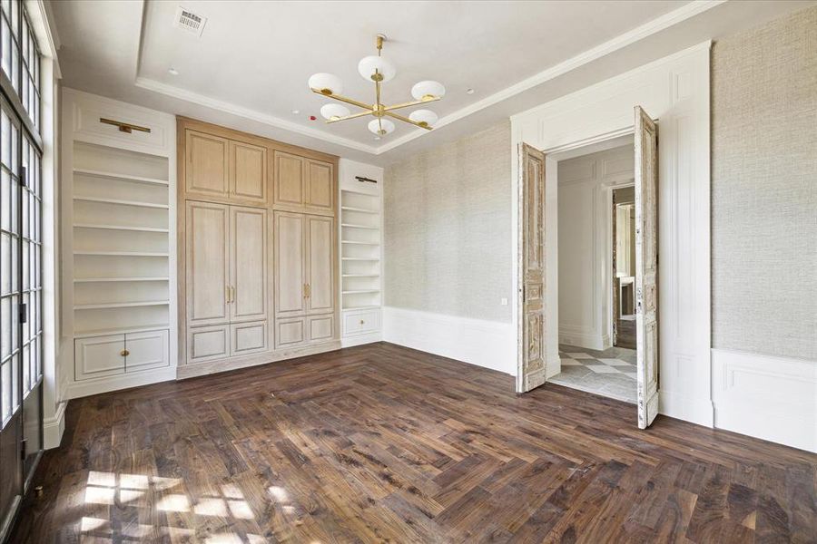 Across the hall from the primary bedroom is the handsome study. The sizable study features a cove ceiling, built in shelving, wood floors, and a swanky gold chandelier.