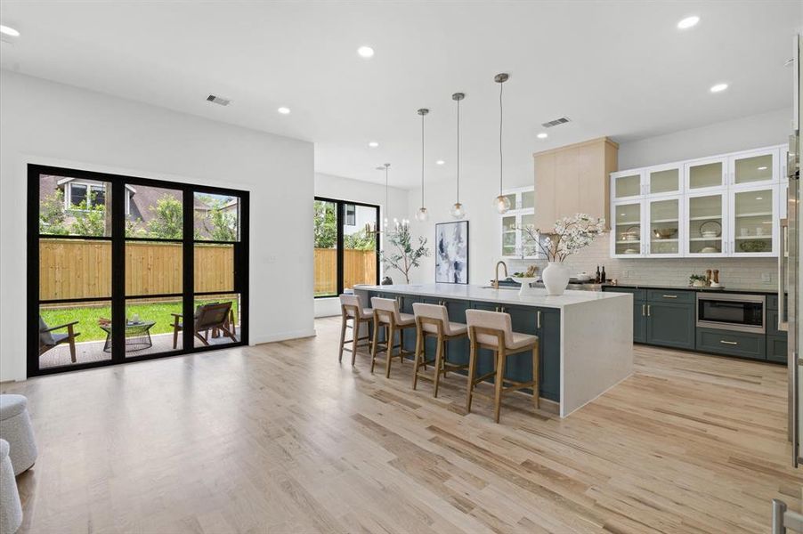 Stunning kitchen featuring oak floors, custom cabinets, a quartz island with seating, and expansive glass doors offering a lush backyard view.