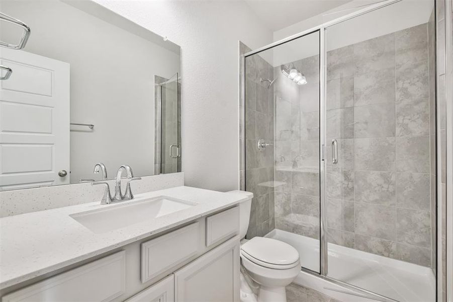 This is a modern, clean-lined bathroom featuring a white vanity with an undermount sink, a large mirror, a glass-enclosed walk-in shower with grey tile, and a white toilet.
