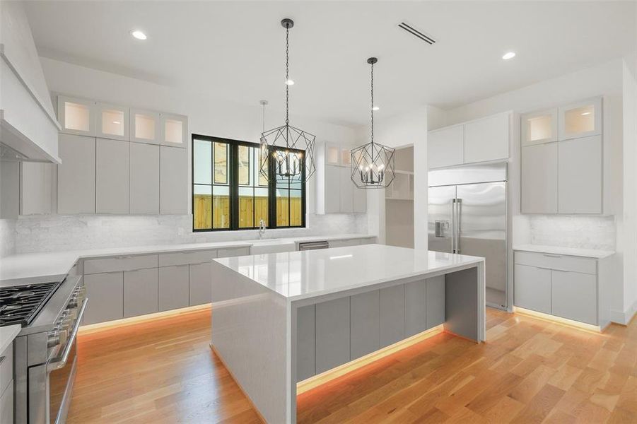 Another view of the island kitchen. storage abound with cabinets on both sides of the island, glass front upper cabinets and large slab front cabinets below. The two pendent lights are supported by undercabinet lighting and recessed LED fixtures. The mud room leads to the garage entry and large walk-in pantry.