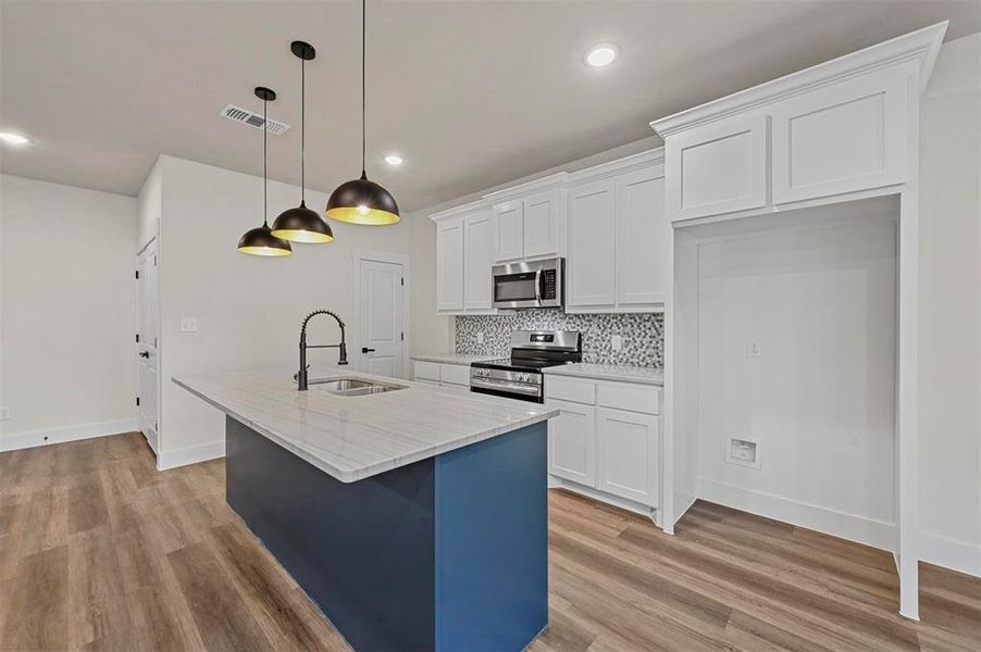 Kitchen with pendant lighting, white cabinets, sink, a kitchen island with sink, and appliances with stainless steel finishes