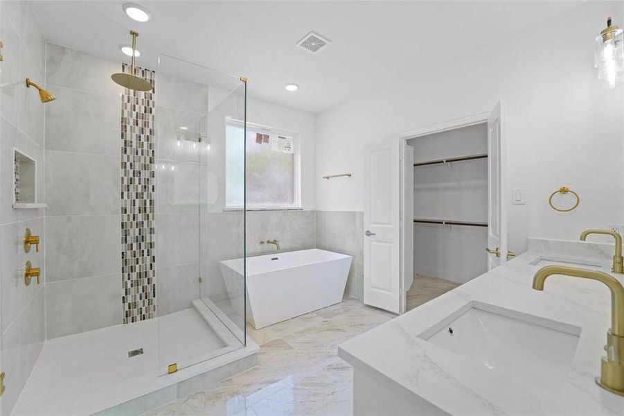 Bathroom with tile walls, tile flooring, independent shower and bath, and dual sinks