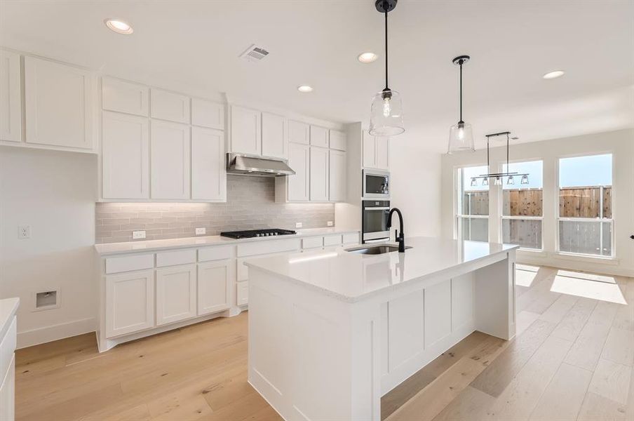 Kitchen featuring an island with sink, sink, pendant lighting, appliances with stainless steel finishes, and light hardwood / wood-style floors