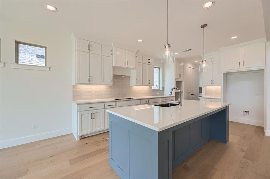 Kitchen featuring backsplash, white cabinetry, an island with sink, light wood-type flooring, and sink