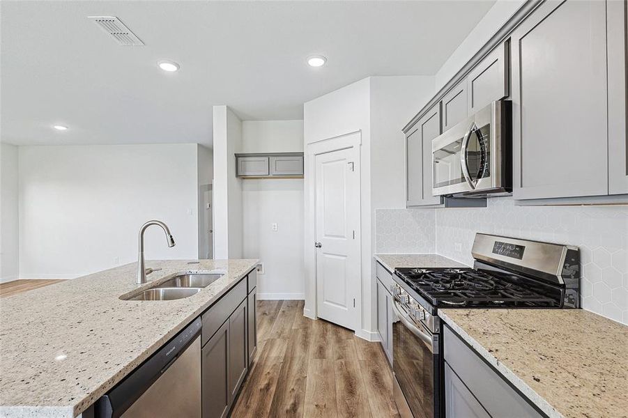 Kitchen with gray cabinetry, appliances with stainless steel finishes, light stone countertops, light hardwood / wood-style floors, and sink