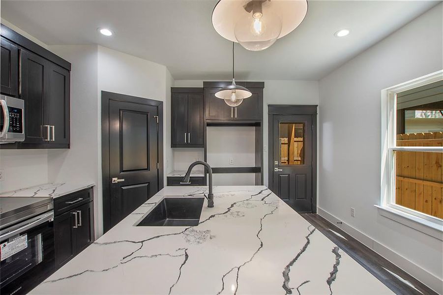 Kitchen featuring sink, hardwood / wood-style flooring, light stone countertops, stove, and pendant lighting