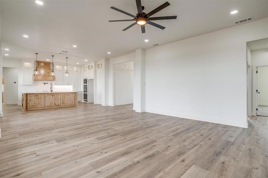 Unfurnished living room featuring ceiling fan, sink, and light wood-type flooring