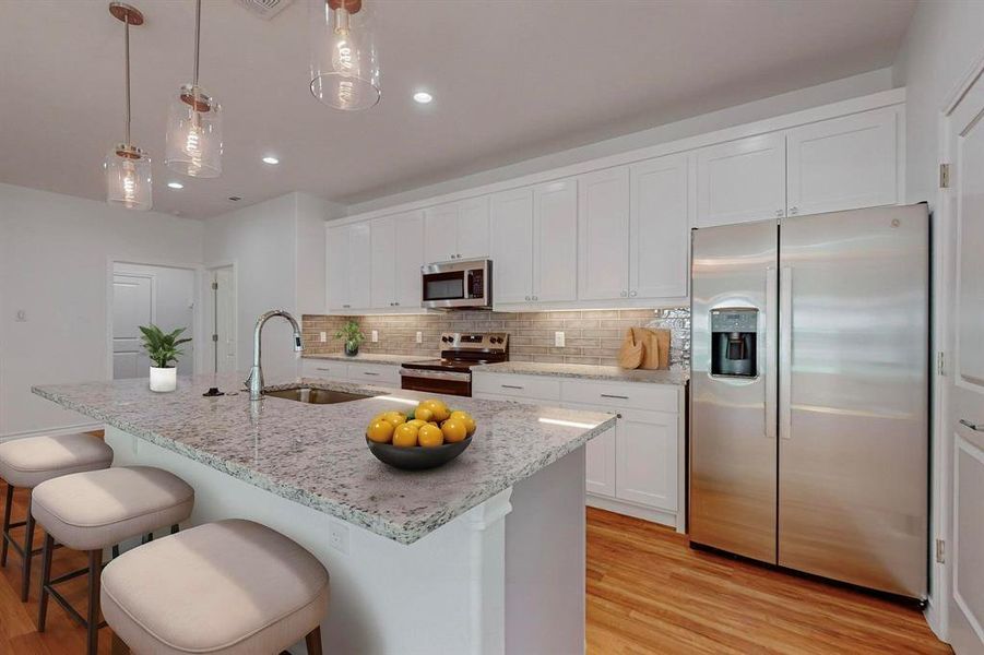 Virtually Staged - Kitchen with appliances with stainless steel finishes, light wood-type flooring, sink, and an island with sink