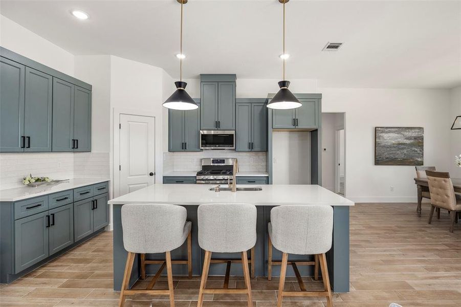 Kitchen featuring light hardwood / wood-style flooring, an island with sink, stainless steel appliances, backsplash, and hanging light fixtures