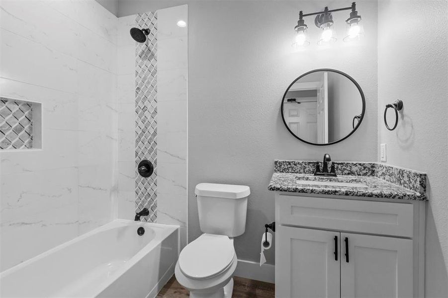 Full bathroom with hardwood / wood-style flooring, tiled shower / bath, toilet, and vanity with extensive cabinet space