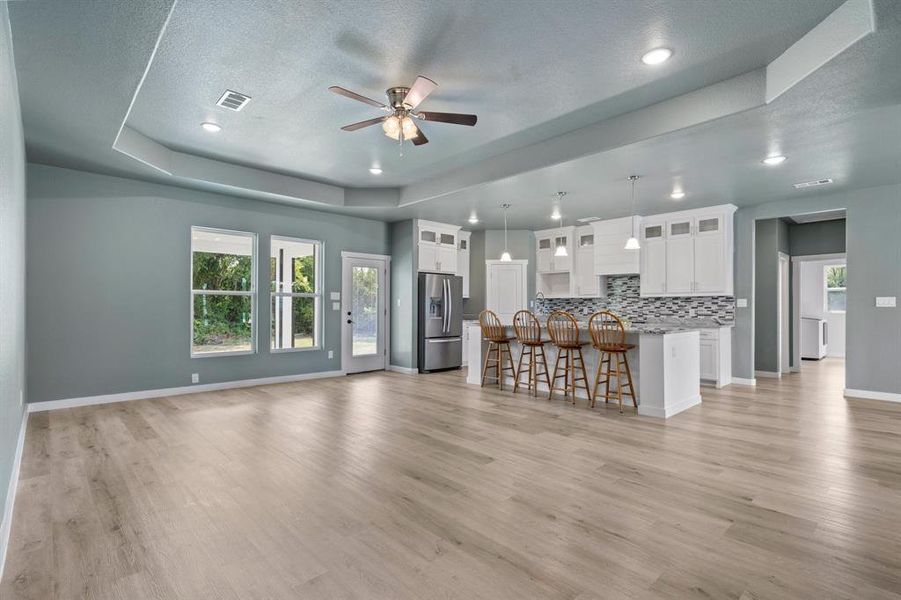 Unfurnished living room featuring a tray ceiling, ceiling fan, indoor bar, and light hardwood / wood-style flooring