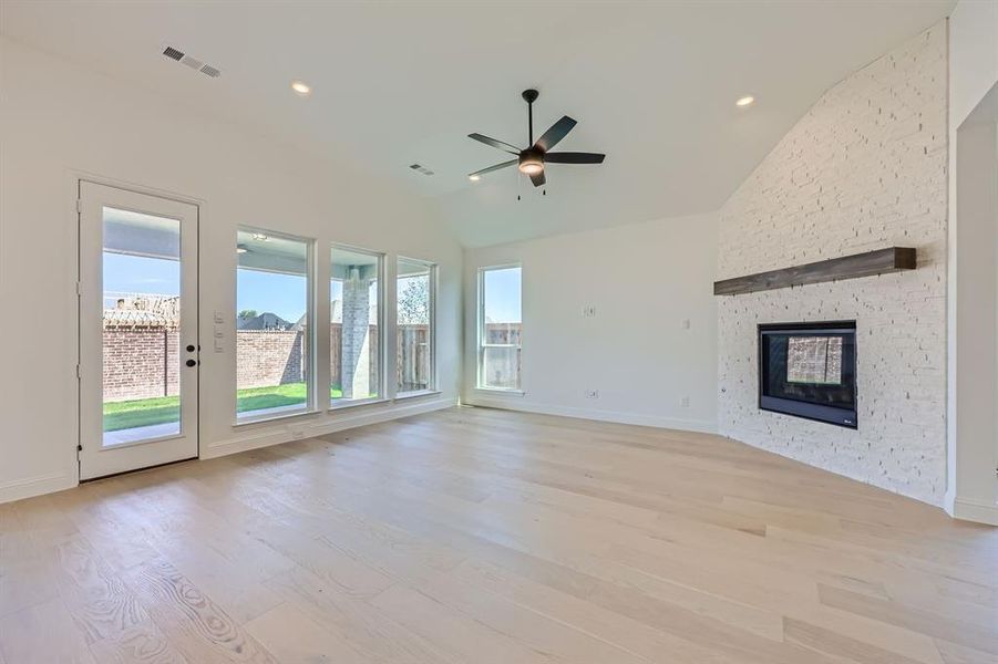 Unfurnished living room with ceiling fan, a fireplace, light wood-type flooring, and lofted ceiling