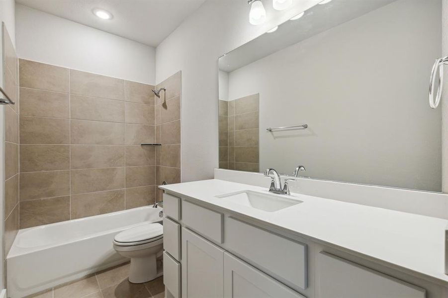Full bathroom with tile flooring, oversized vanity, toilet, and tiled shower / bath combo