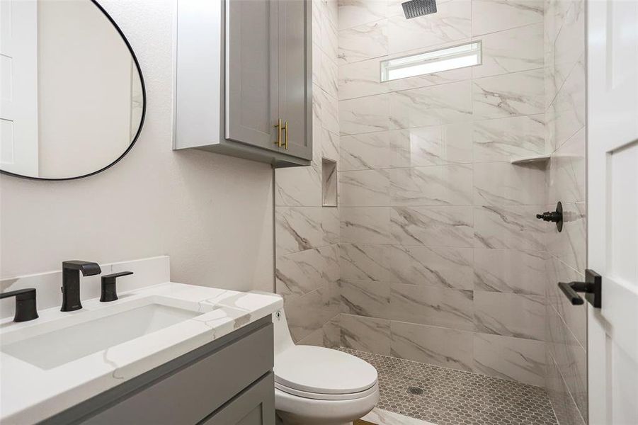 Bathroom featuring vanity, tiled shower, and toilet