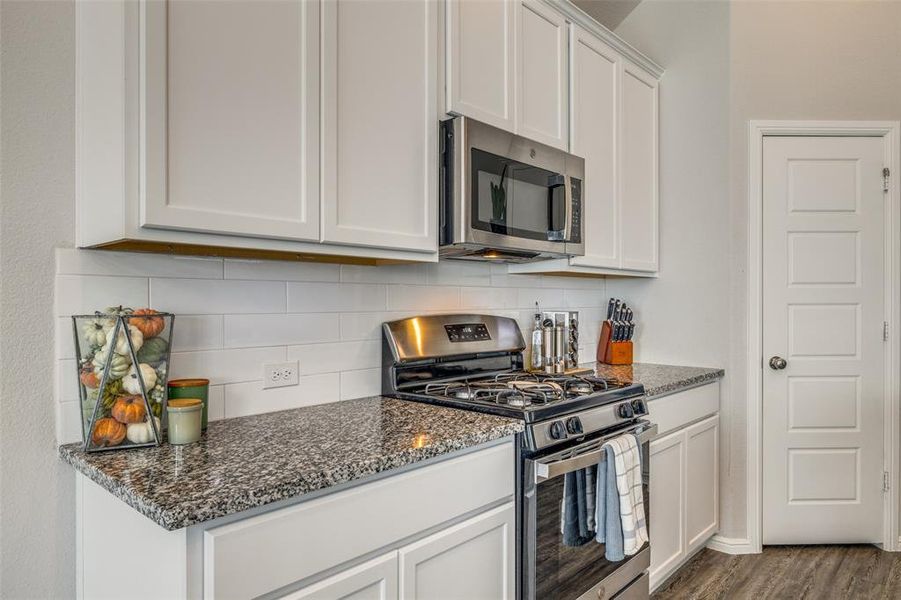 Kitchen featuring granite counters, white cabinetry, backsplash, appliances with stainless steel finishes, and wood-style flooring