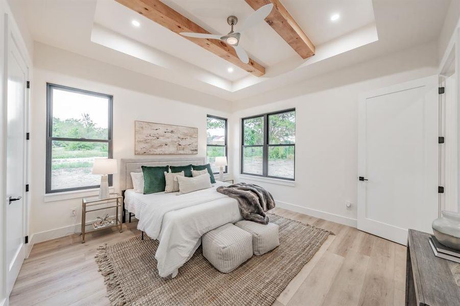 Bedroom with beam ceiling, a tray ceiling, blonde plank, wood-like luxury vinyl floors.