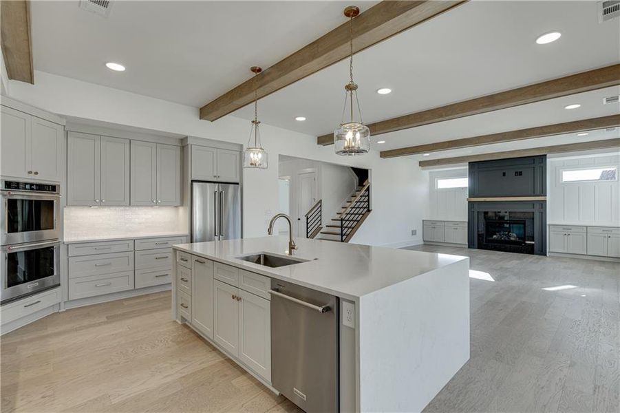 Kitchen with sink, pendant lighting, stainless steel appliances, light wood-type flooring, and an island with sink