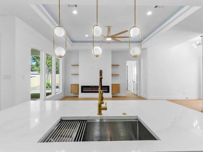 Kitchen with light hardwood / wood-style floors, a raised ceiling, light stone countertops, decorative light fixtures, and sink