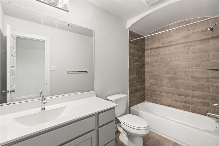 Secondary bath features tile flooring, bath/shower combo with tile surround, light stained wood cabinets, beautiful light countertop. Sample photo of completed home with similar floor plan. As-built interior colors and selections may vary.