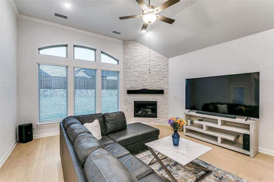 Living room featuring a fireplace, hardwood / wood-style floors, ceiling fan, lofted ceiling, and crown molding