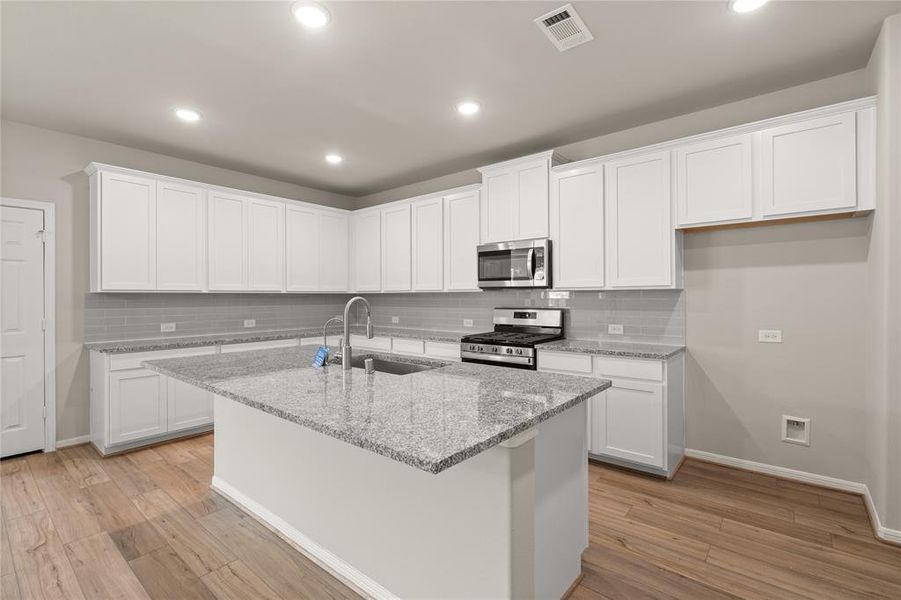 This light and bright kitchen features a large quartz island, white cabinets, a large sink overlooking your family room, recessed lighting, and beautiful backsplash.