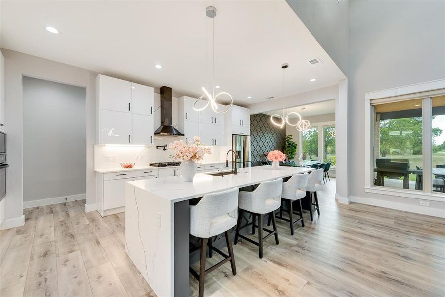 Kitchen featuring pendant lighting, an island with sink, white cabinetry, wall chimney exhaust hood, and an inviting chandelier