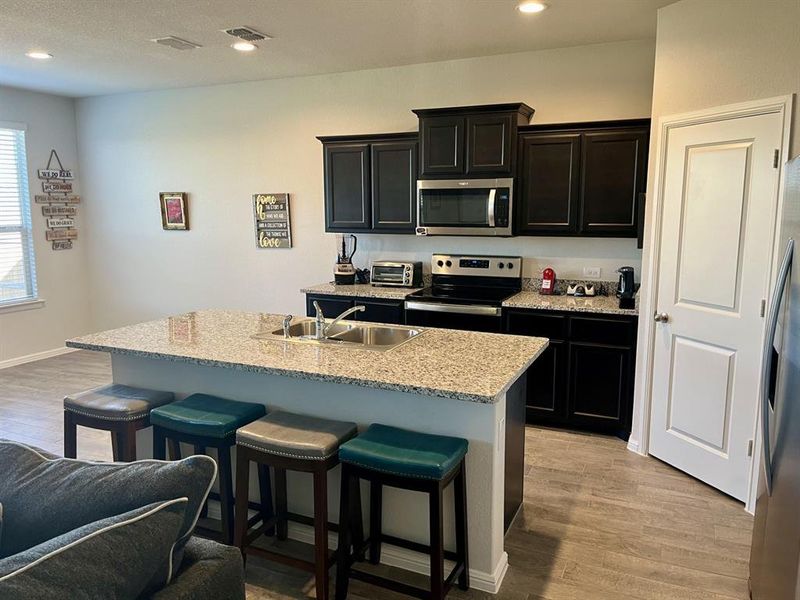 Kitchen featuring stainless steel appliances, light hardwood / wood-style floors, a center island with sink, and sink