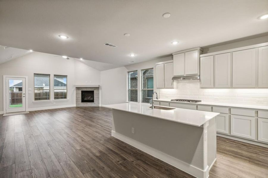 Kitchen featuring vaulted ceiling, stainless steel gas stovetop, an island with sink, sink, and hardwood / wood-style flooring