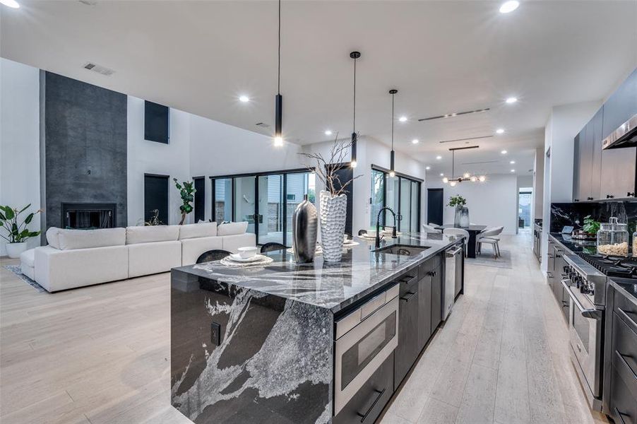 Kitchen featuring appliances with stainless steel finishes, sink, a large island, pendant lighting, and dark stone countertops