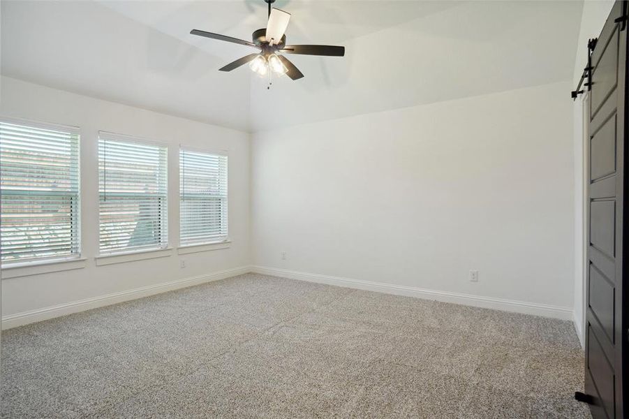 Unfurnished bedroom with carpet floors, multiple windows, ceiling fan, and a barn door