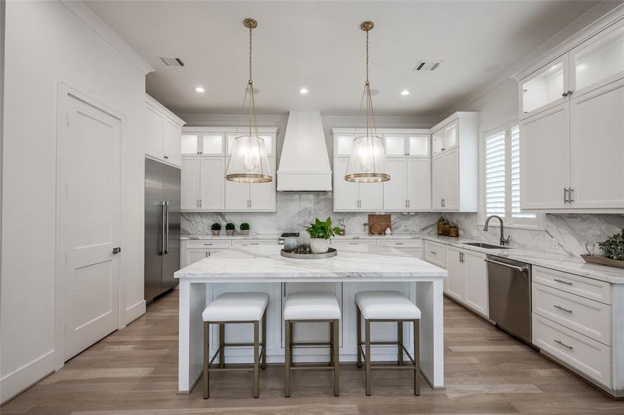 This designer island kitchen features marble, Sub Zero and Thermador appliances, custom light fixtures, plentiful storage plus pantry, and a breakfast bar that accommodates three people.