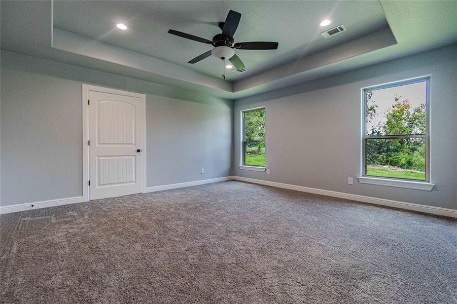 Empty room with a tray ceiling, carpet floors, and ceiling fan